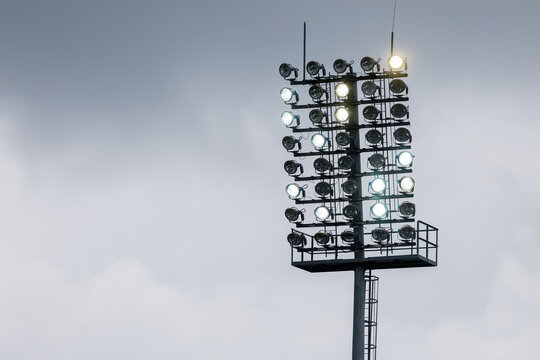Sport stadium light mast with glowing spotlights on a rainy day