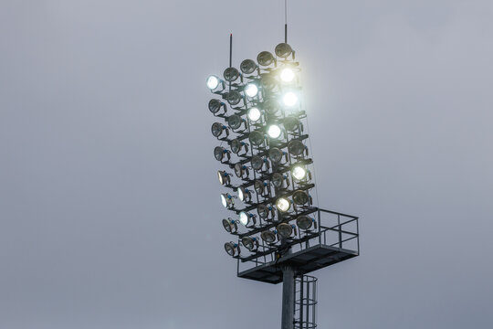 Sport stadium light mast with glowing spotlights on a rainy day