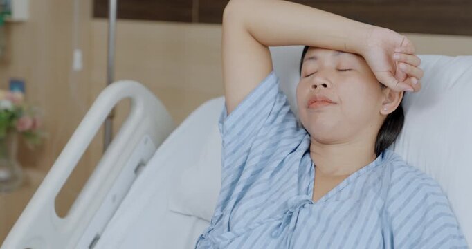 Asian female patient is holding her arm over her head in hospital room, she is anxious and stressed during treatment.