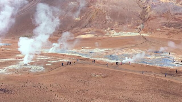 Tourists walking through the barren landscape of the Hverir geothermal area in Iceland, observing hot springs and fumaroles emitting steam