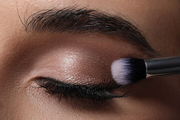 Naklejka premium Applying eye shadow with brush onto woman's face, closeup