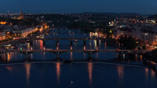 Aerial drone view of multiple Vltava river bridges lit at night with city streets glowing in the blue hour, Prague, Czech Republic.