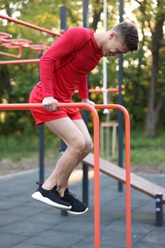 Athletic young man exercising on parallel bars at outdoor gym, low angle view