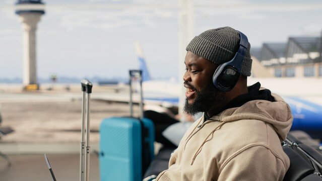 African american man on video conference call using airport internet, speaking to colleagues during online meeting while seated in the terminal waiting area, digital communication and mobility.