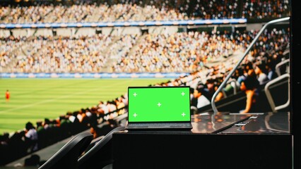 Mockup green screen laptop in a crowded stadium during football game, fans cheering in tribunes...