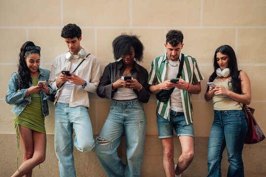 Young diverse friends standing together, ignoring each other, focusing on smartphones, representing digital addiction and phubbing