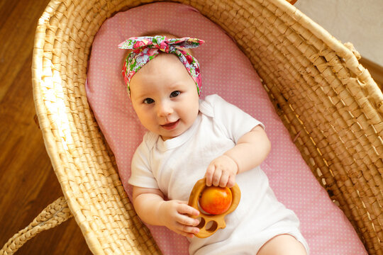 Smiling baby girl lying in wicker bassinet holding wooden teether toy