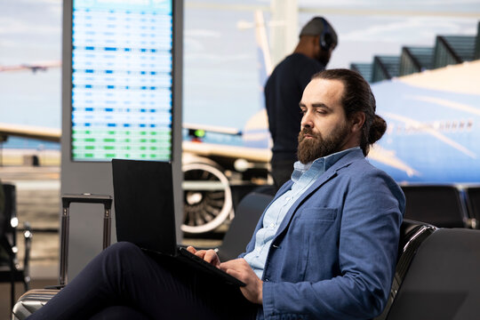 Modern businessman working on laptop in airport lounge near gate, traveling abroad via international flight for multinational company, traveler representing global business, featuring business trip.