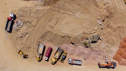 Construction site with heavy machinery including multiple dump trucks and excavators moving soil and rubble, engaged in earthworks and industrial groundwork creation © Nasos Zovoilis