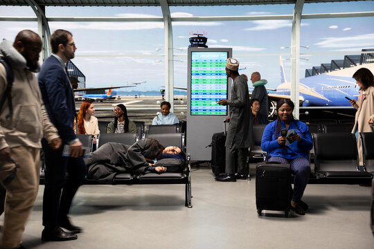 Sleeping, jet lag and woman on airport bench next to people checking flight schedule screen, napping, city break and Tired tourist on chair in departure terminal traveling internationally.