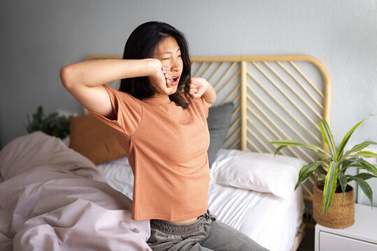 Asian woman waking up in bed yawning and stretching