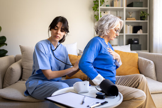 Nurse visiting elderly woman at home using stethoscope for lung examination