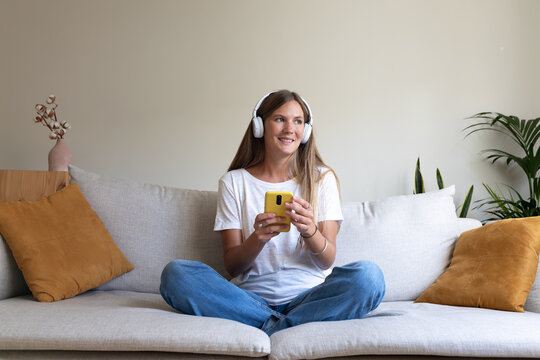 Young woman relaxing on sofa listening to music with headphones and smartphone