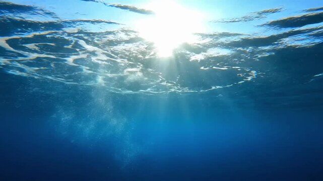 Sunlight rays shine through the ocean surface and create patterns of light under the water surface during midday