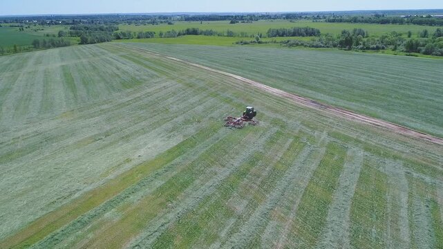 Drone flying backward and upward over tractor in field