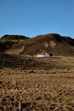 Lone blue house with red roof in a rugged volcanic mountain landscape