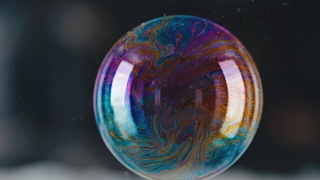 Close-up macro photography of a swirling iridescent soap bubble floating against a dark blurred background showing beautiful fluid colors