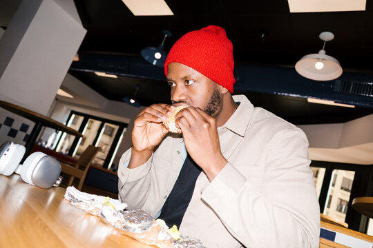 Young man eating hamburger in fast food restaurant