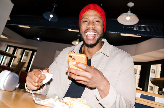 Happy black man enjoying lunch checking phone