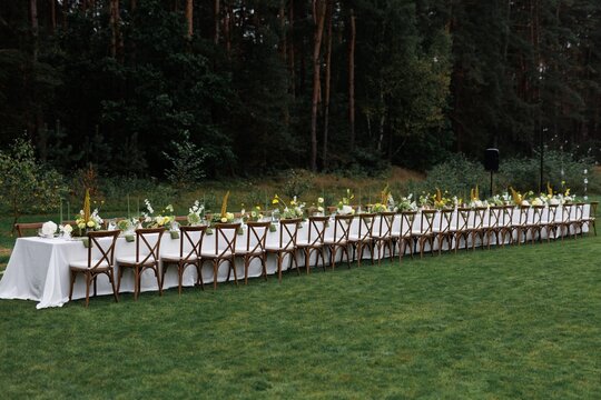 Long decorated table with flowers, candles and cutlery near forest