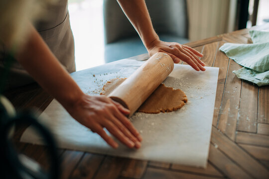 Side view of rolling dough with wooden pin on floured surface