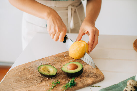Cutting fresh lemon on wooden board with avocado halves