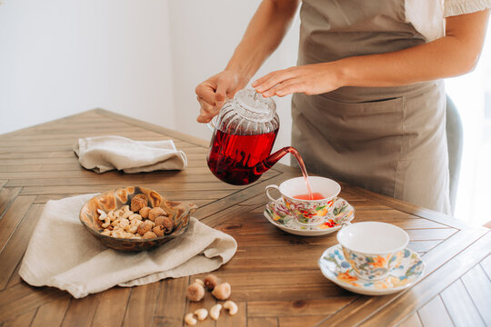 Woman pouring herbal tea from glass teapot into floral cup