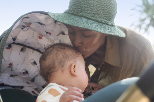 Mother Kisses Baby on Forehead in Sunny Park