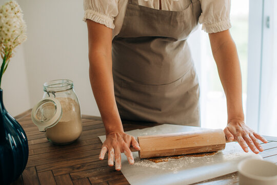 Woman rolling dough with wooden rolling pin on floured surface