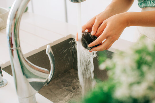 Washing fresh avocado under running water in modern kitchen sink
