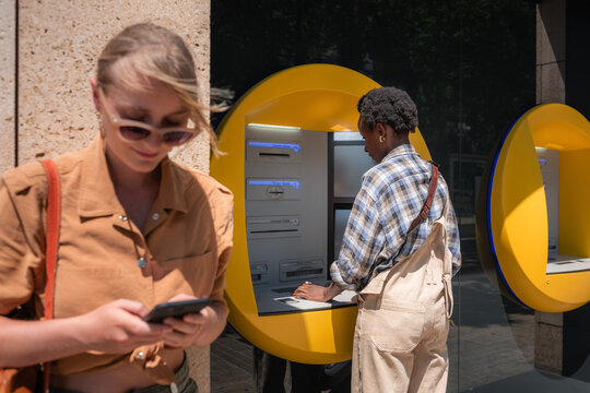 Woman using smartphone while waiting for friend using ATM 