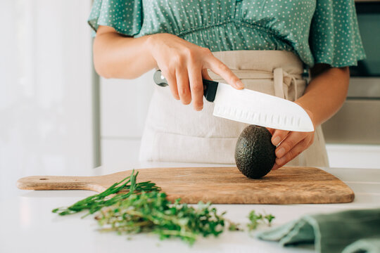 Female hands slicing avocado with knife on wooden cutting board
