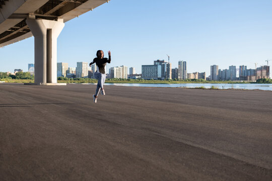 Black female runner leaping under bridge