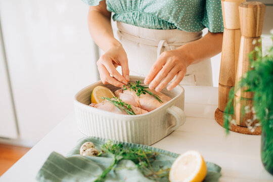 Woman arranging fresh herbs on raw chicken in ceramic baking dis