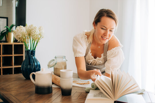 Woman checking recipe book while preparing dough in kitchen