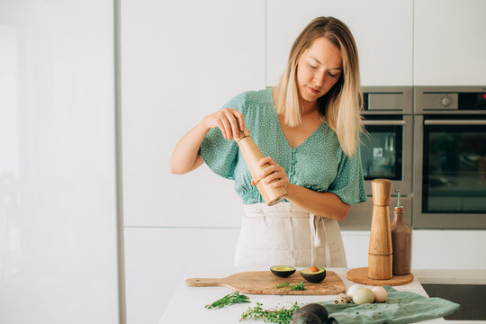 Woman seasoning avocado with pepper mill in modern kitchen