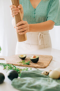 Close-up of hands grinding pepper over avocado halves on cutting