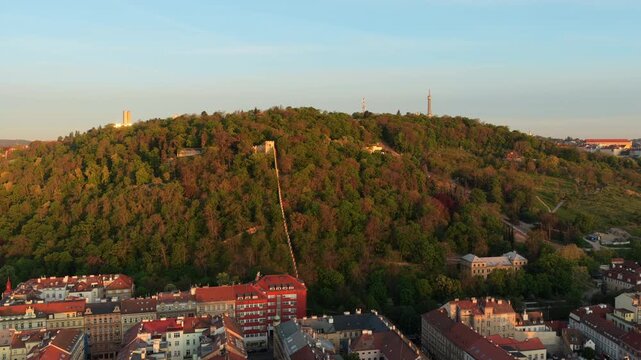 Aerial drone view of Petrin hill covered in spring green forest with the funicular track and Petrin tower visible at the summit, Prague, Czech Republic.