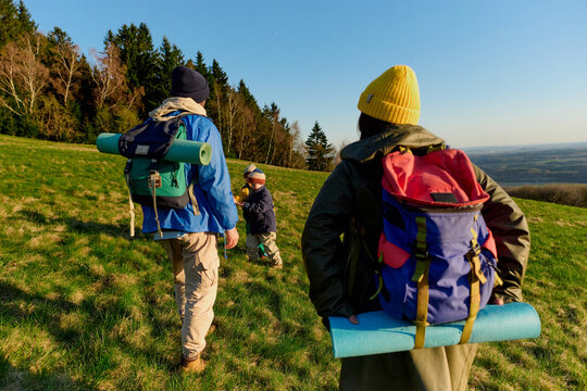 Family hiking with backpacks across sunny hillside