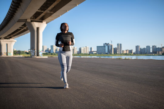 Black sportswoman running under bridge