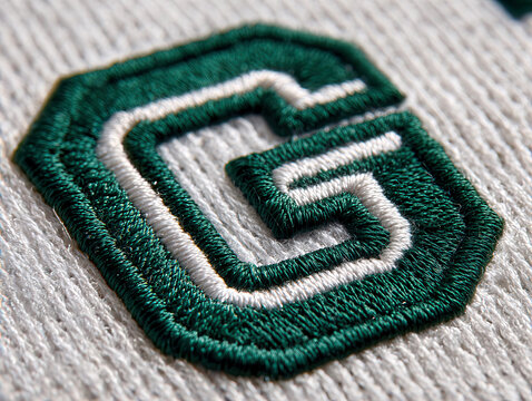 Close-up of a stitched college-style G emblem in forest green and white on a white background, possibly sports attire fabric Realistic style with shallow depth of field, soft and diffu - AI-Generated