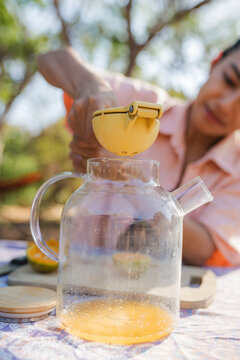 Hand squeezing fresh orange juice outdoors into glass pitcher