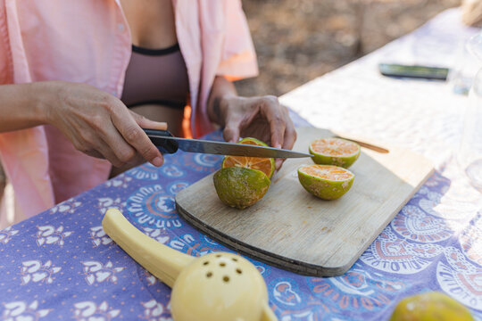 Hands slicing citrus fruit on wooden cutting board