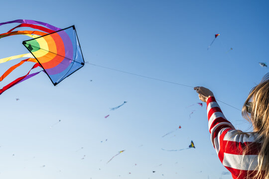 Young woman flying a colorful kite with numerous kites in sky