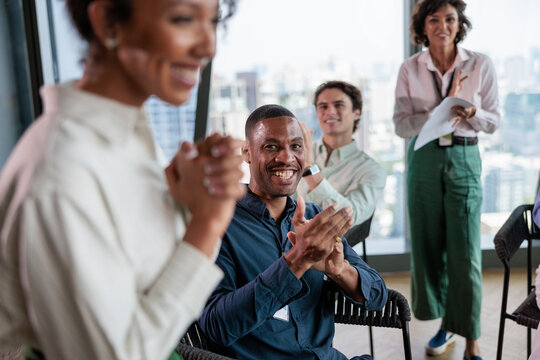 Diverse group applauds presenter in modern office setting.