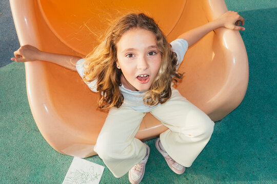 Close up of girl inside orange playground slide looking at camera