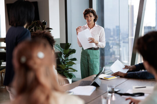 Businesswoman presents documents to colleagues in a modern office.
