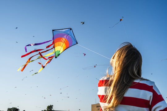 Young woman flying a colorful kite with numerous kites in sky