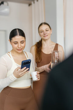 Woman on background looking at female with cup using smartphone