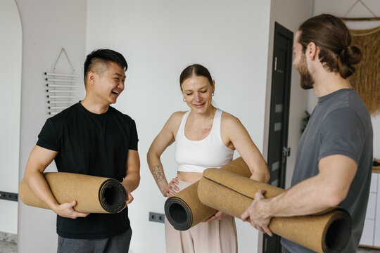 Happy men and woman holding sports carpets and meeting before training